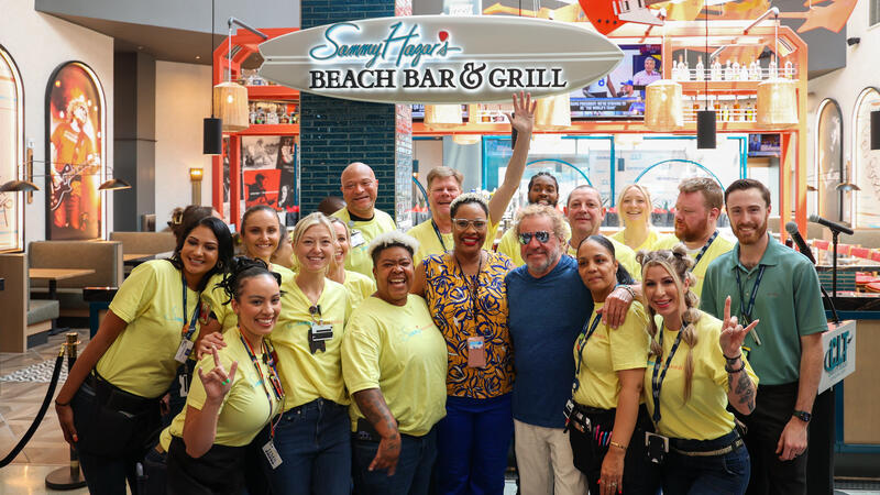 A group of associates posing in front ot a signboard of a restaurant.