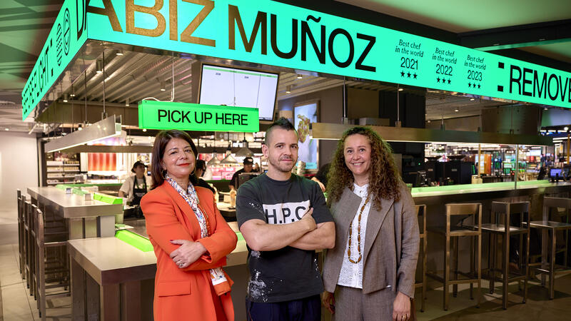 Three people, one man and two women in front of a counter of a restaurant.