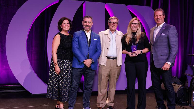 Five people, 3 men and a 2 women on a stage receiving an award.