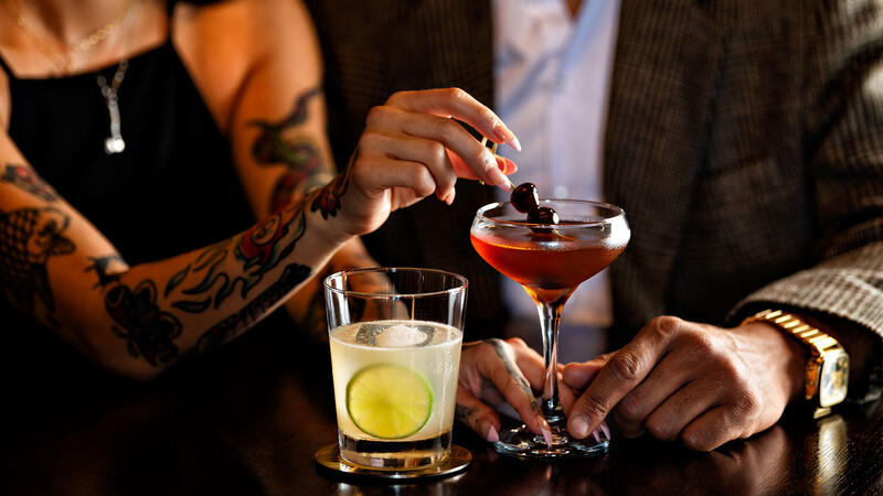 A couple drinking cocktails at the bar.