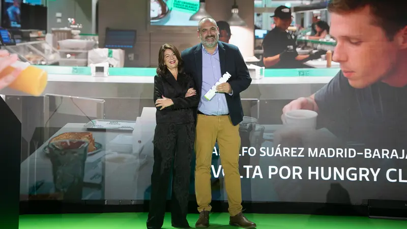A man and a woman receiving a trophy award on a stage