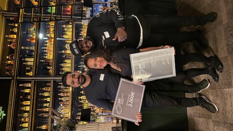 three people smiling and holding a certificate awards in front of a bar counter