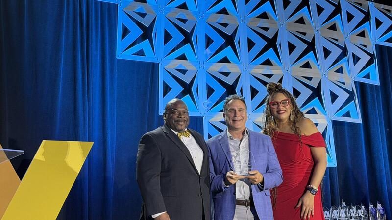 Two men and one woman on a stage receiving an award