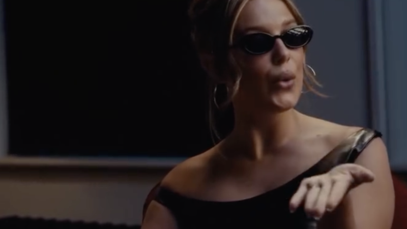 A blonde woman wearing a black dress and sunglasses sitted at a table