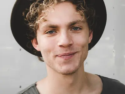 a young man with blond curly hair and a hat