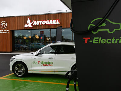 An electric car charging at a station located in front of the entrance to an Autogrill store.