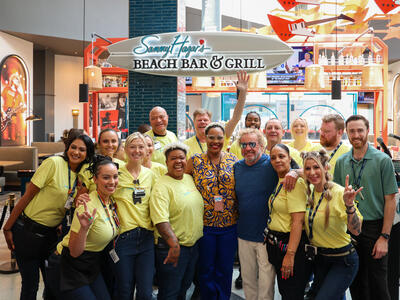 A group of associates posing in front ot a signboard of a restaurant.