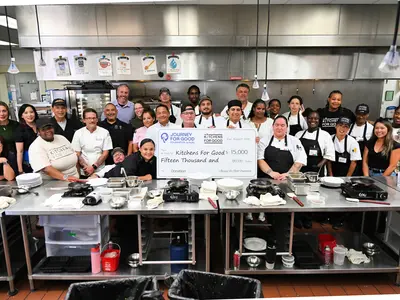 A kitchen team holding a large donation cheque