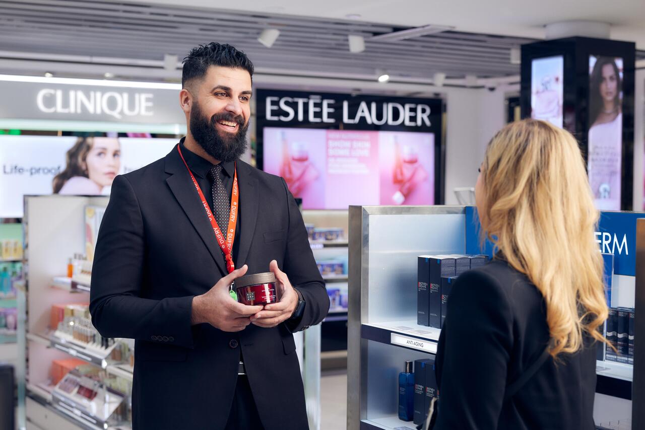 A smiling man showing a cream to a female customer.