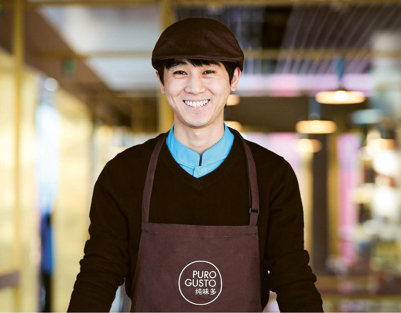 A smiling asian male employee wearing a Puro Gusto's apron