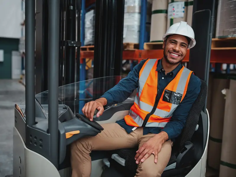 A boy wearing a safety helmet on a forklift.
